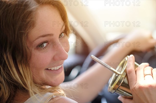 Woman driving and drinking from gold cup