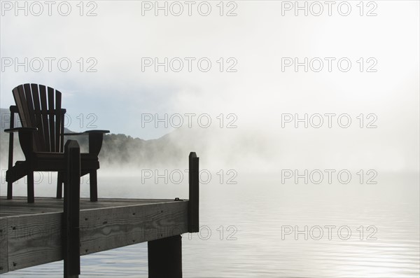 USA, New York, St Armand, Empty chair on jetty by Lake Placid at dawn
