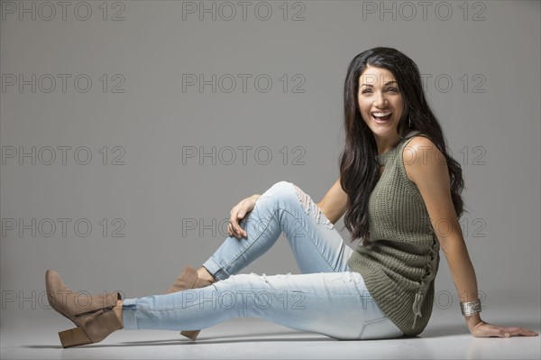 Studio shot of woman sitting on floor and laughing