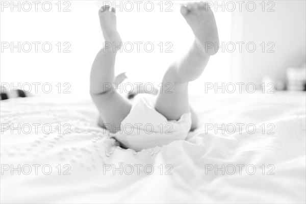 Baby girl (6-11 Months) lying down on bed with feet in air