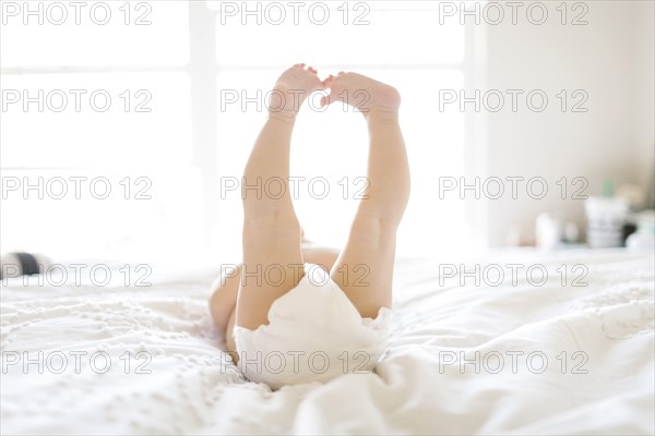 Baby girl (6-11 Months) lying down on bed with feet in air