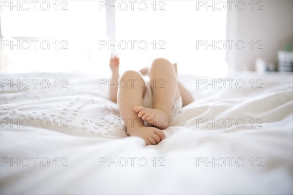Portrait of baby girl (6-11 Months) lying down on bed with barefoot
