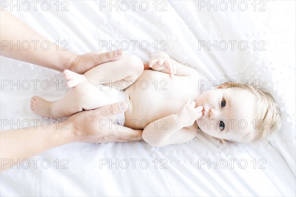 Baby girl (6-11 Months) lying down with finger in mouth while father holding her, directly above