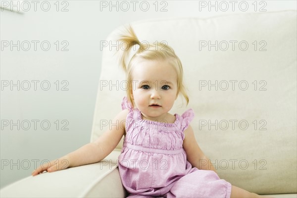 Portrait of baby girl (12-17 months) sitting on sofa