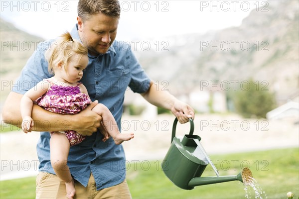 Father with baby girl (12-17 months) watering plants in backyard