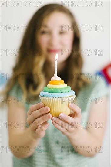 Mid adult woman holding cupcake with birthday candle