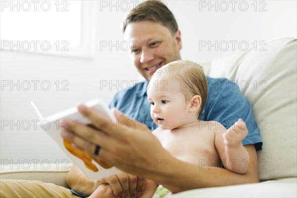 Father with baby girl (12-17 months) sitting in living room and reading book
