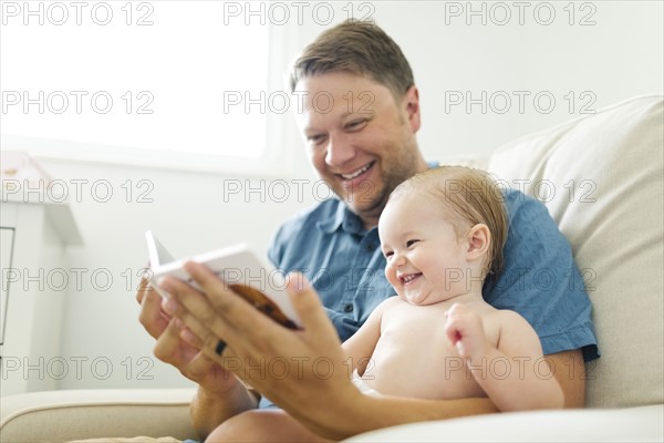 Father with baby girl (12-17 months) sitting in living room and reading book