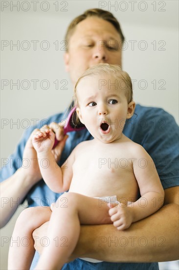 Father and baby girl (12-17 months) brushing hair after bath