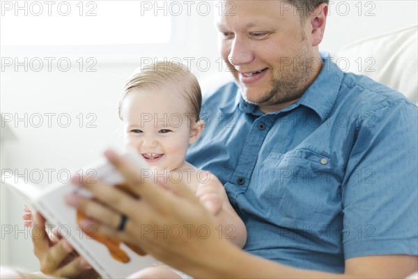 Father with baby girl (12-17 months) sitting in living room and reading book