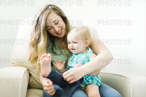 Mother dressing daughter (11-17 months) in living room