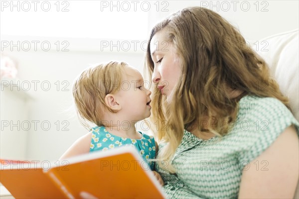 Mother with baby girl (12-17 months) sitting in living room and reading book