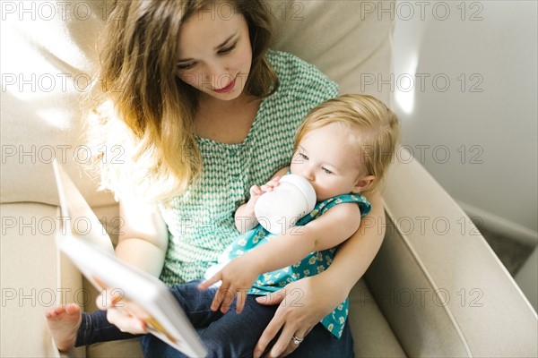 Mother with baby girl (12-17 months) sitting in living room and reading book
