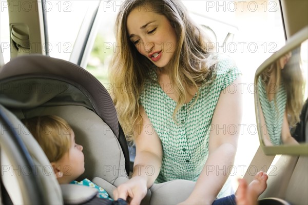 Mother preparing baby girl (12-17 months) for car trip