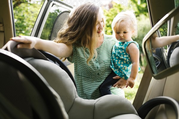 Mother preparing baby girl (12-17 months) for car trip