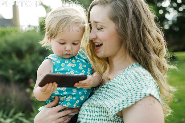 Mother carrying daughter (12-17 months), daughter playing on smartphone