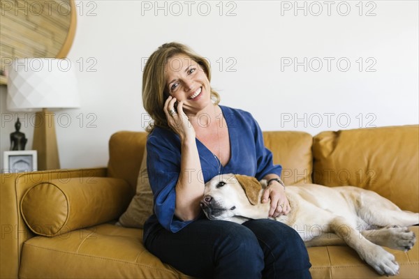 Woman stroking Labrador Retriever and using mobile phone