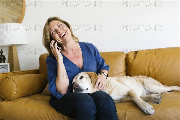 Woman stroking Labrador Retriever and using mobile phone