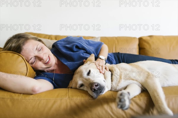 Woman and Labrador Retriever lying down on sofa