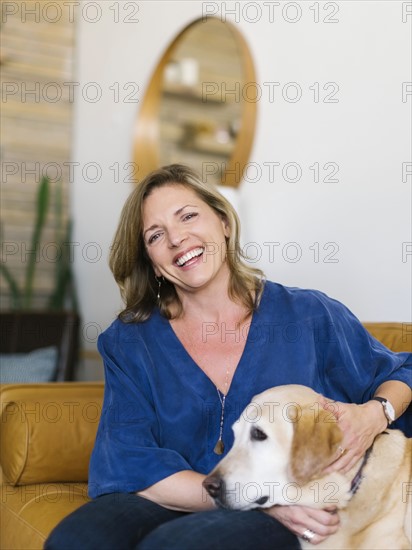 Portrait of woman stroking Labrador Retriever on sofa