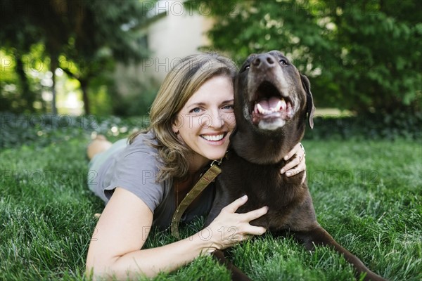 Portrait of smiling woman lying on grass with Labrador Retriever