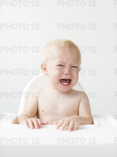 Portrait of baby boy (12-17 months) sitting in high chair and crying