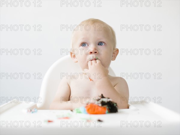 Baby boy (12-17 months) sitting in high chair and eating cupcake