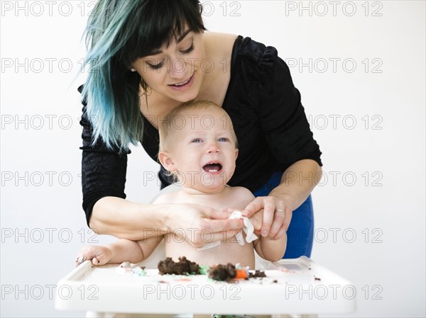 Mother cleaning baby boy (12-17 months) from cupcake