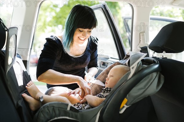 Mother fastening baby boy (12-17 months) in car seat