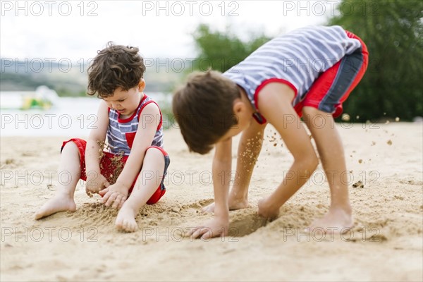 Brothers (4-5, 6-7) playing on beach by lake