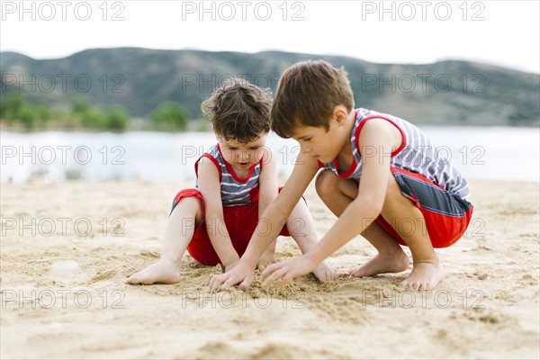 Brothers (4-5, 6-7) playing on beach by lake