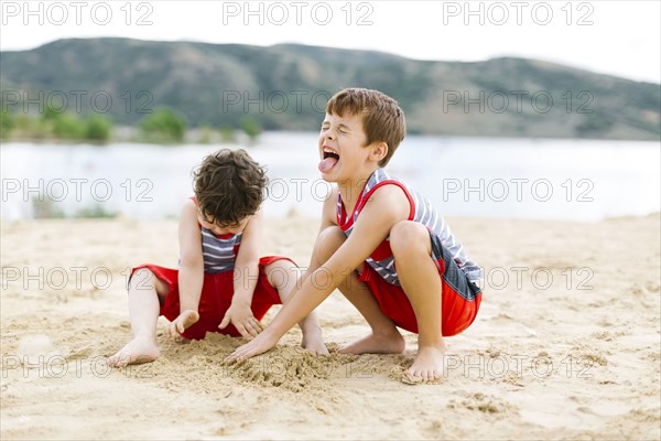 Brothers (4-5, 6-7) playing on beach by lake