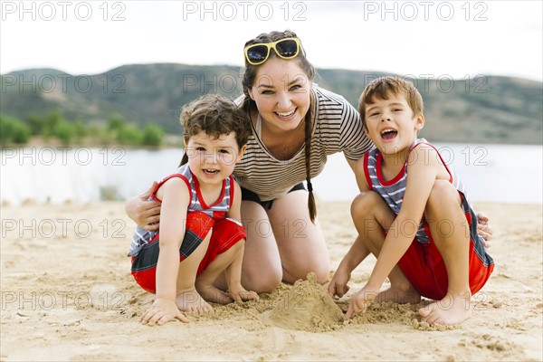 Mother playing with sons (4-5, 6-7) on beach by lake