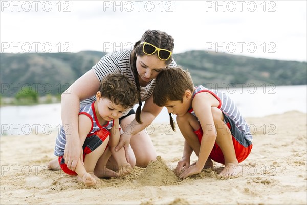 Mother playing with sons (4-5, 6-7) on beach by lake