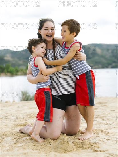 Mother playing with sons (4-5, 6-7) on beach by lake