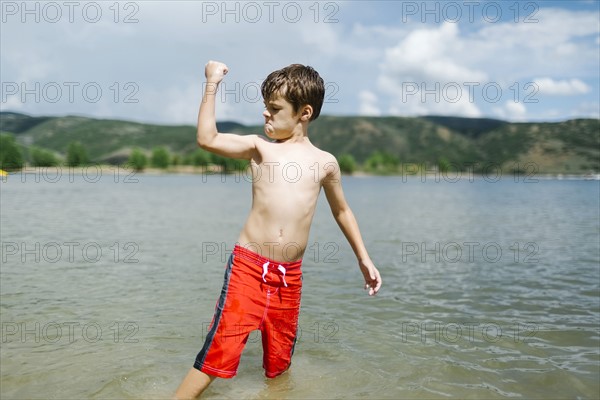 USA, Utah, Park City, Boy (6-7) flexing muscles while wading in lake