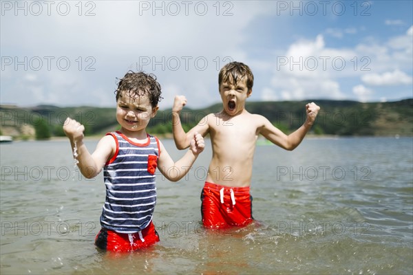 USA, Utah, Park City, Brothers (4-5, 6-7) flexing muscles while wading in lake