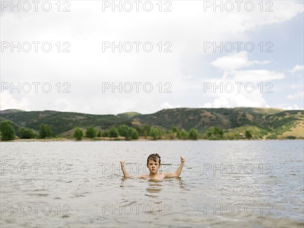USA, Utah, Park City, Boy (6-7) flexing muscles in lake