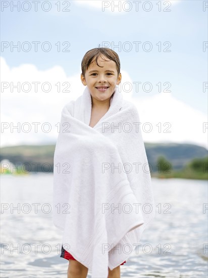 Portrait of boy (6-7) wrapped in towel standing by lake