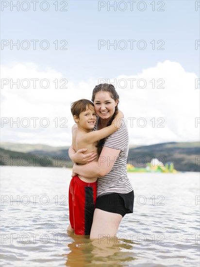 Mother with son (6-7) embracing while wading in lake