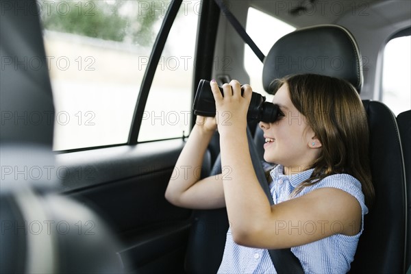 Girl ( 8-9) sitting in car and looking through binoculars