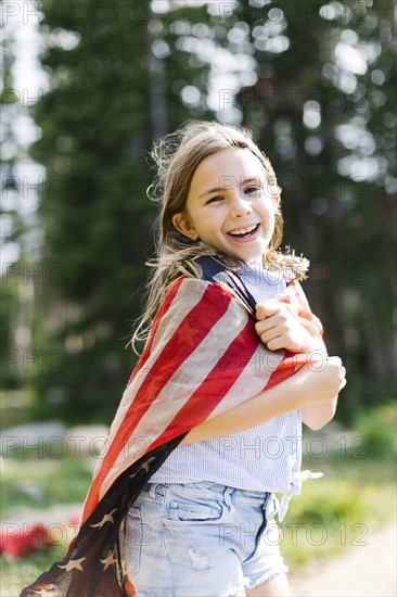 Portrait of girl (8-9) wrapped in us flag in forest