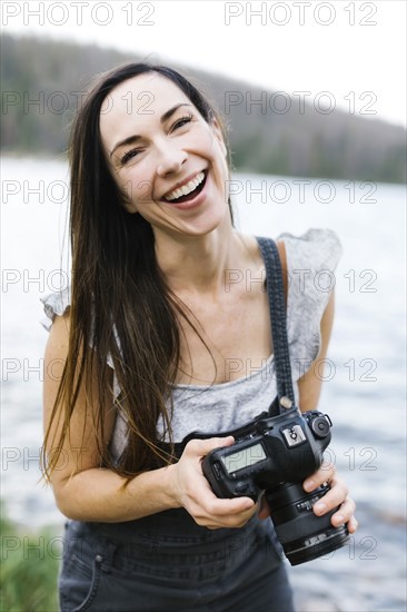 Portrait of woman holding camera by lake