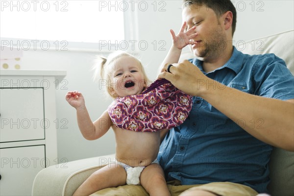 Father dressing daughter (12-17 months)