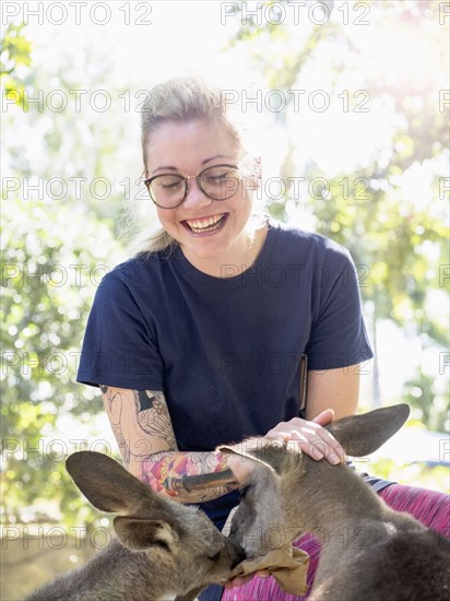 Young woman feeding Eastern grey kangaroos (Macropus giganteus) and smiling