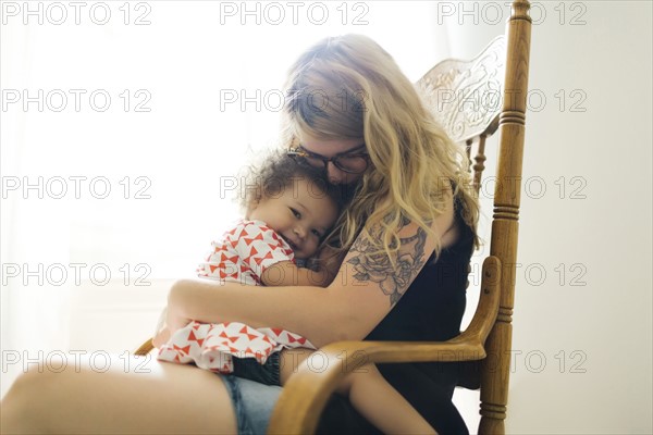 Mother sitting on chair and rocking daughter (12-17 months)