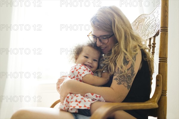 Mother sitting on chair and rocking daughter (12-17 months)