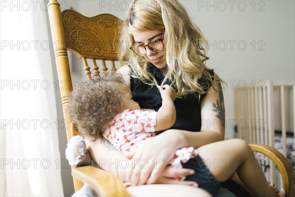 Mother sitting on chair and breastfeeding daughter (12-17 months)