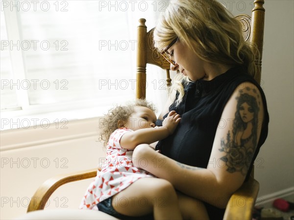 Mother sitting on chair and breastfeeding daughter (12-17 months)