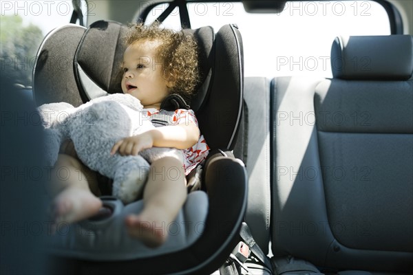 Girl (12-17) sitting on car seat and holding plush toy